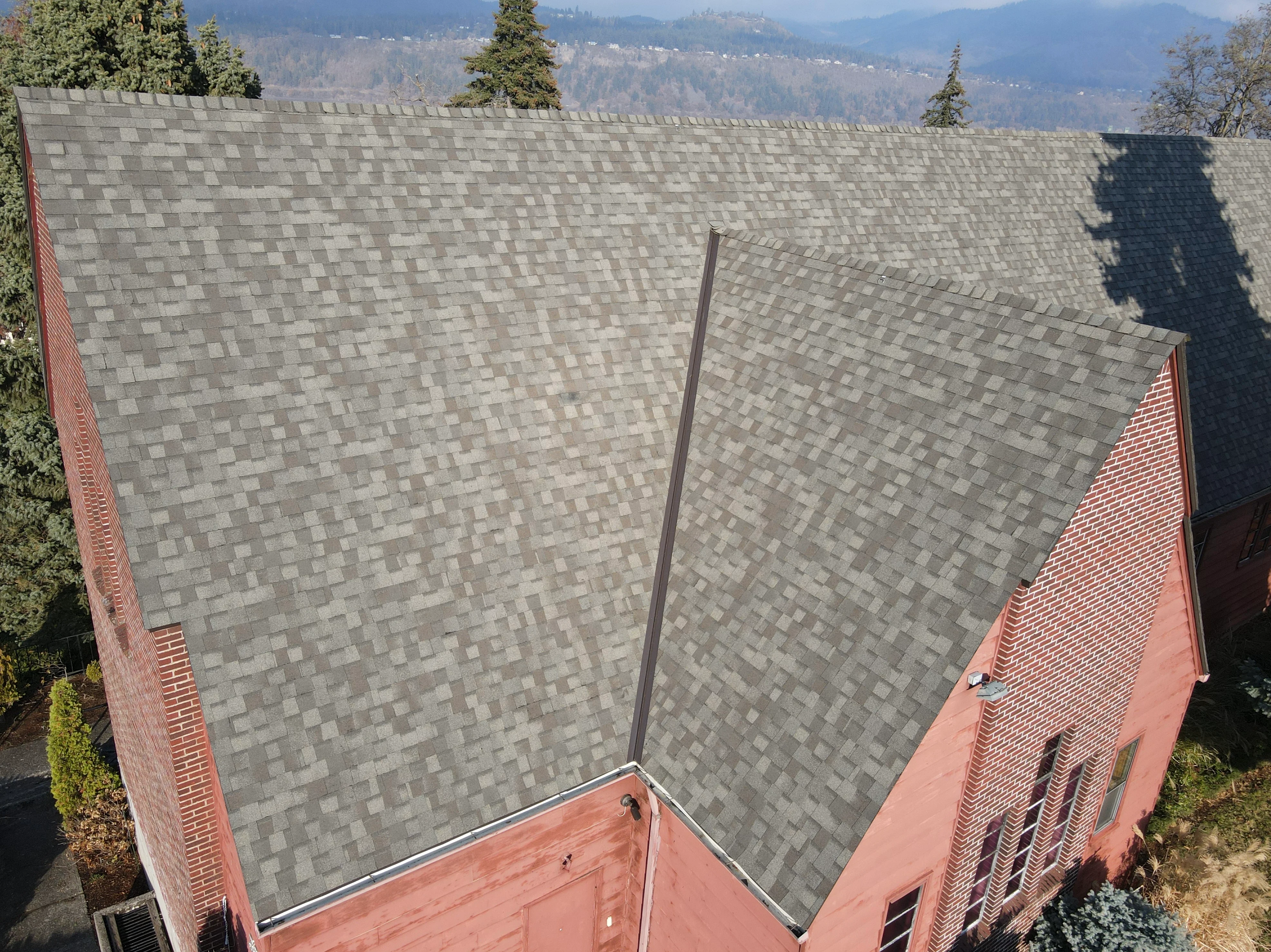 Gray architectural shingles installed on multi-pitched residential roof with brick chimney