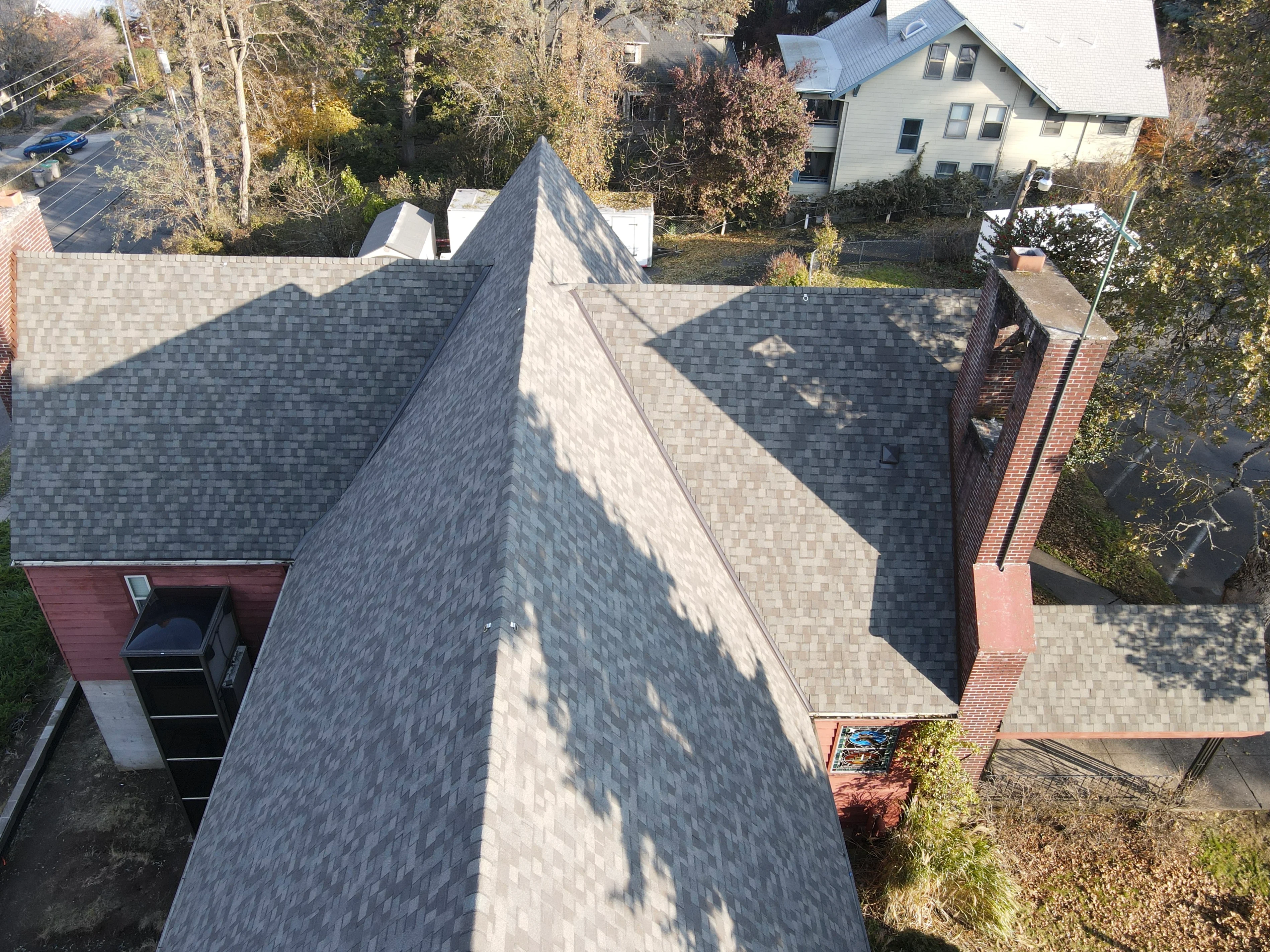 Gray architectural shingles installed on residential roof with multiple planes and brick chimney