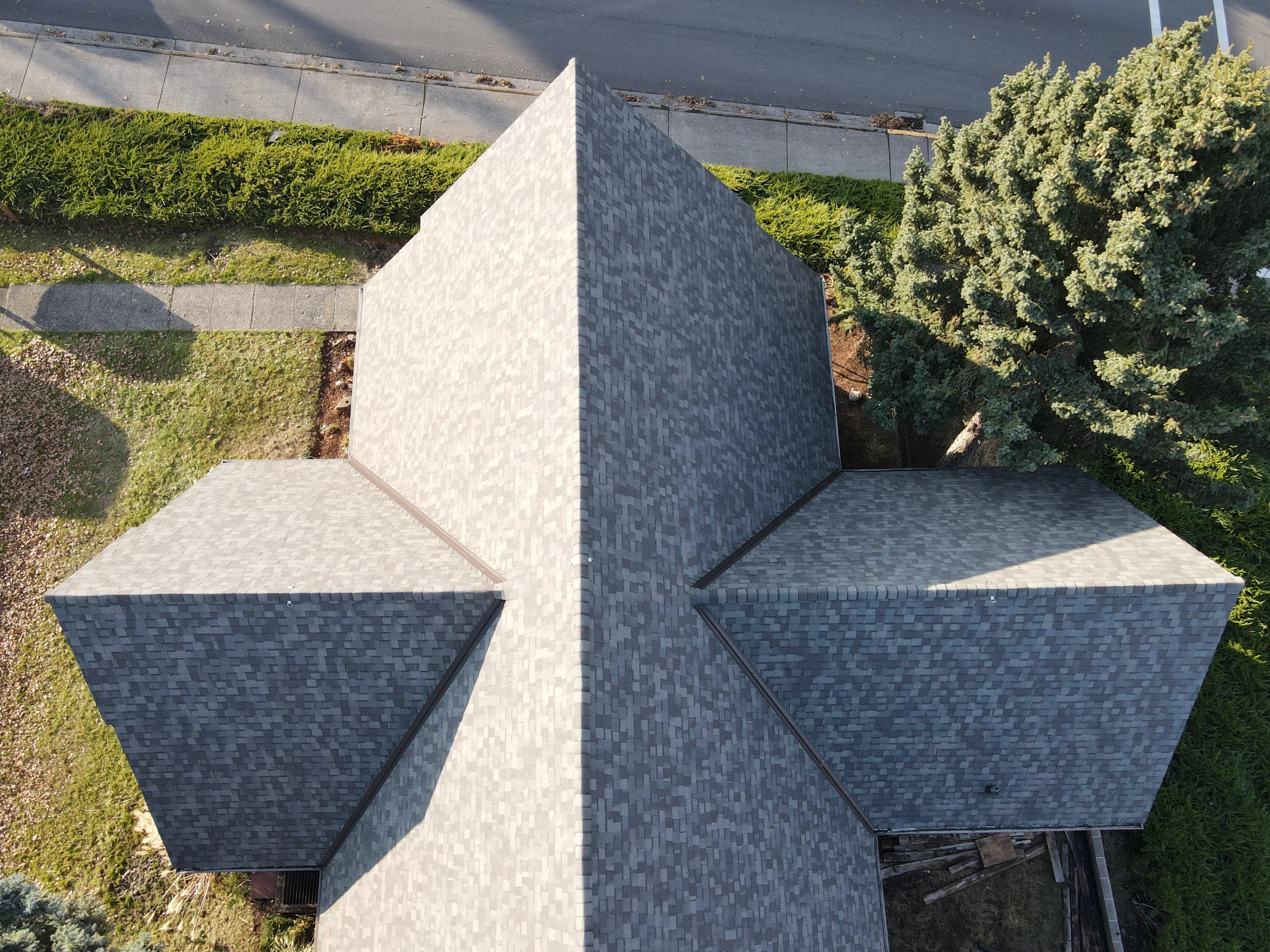 Aerial view of charcoal gray asphalt shingle roof on geometric structure with multiple angled planes