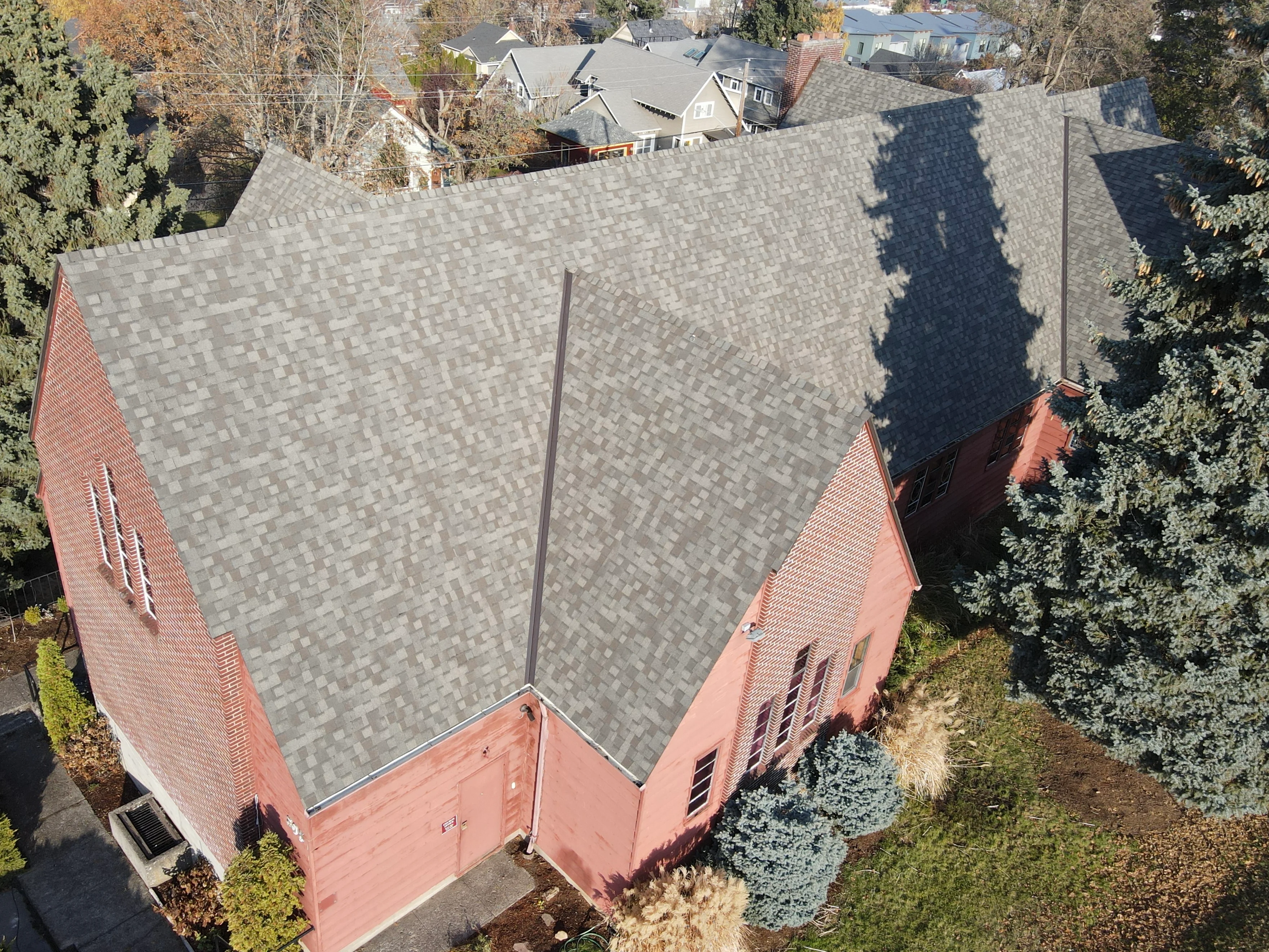 Gray architectural shingles on multi-pitched roof with brick chimney and red brick gable ends